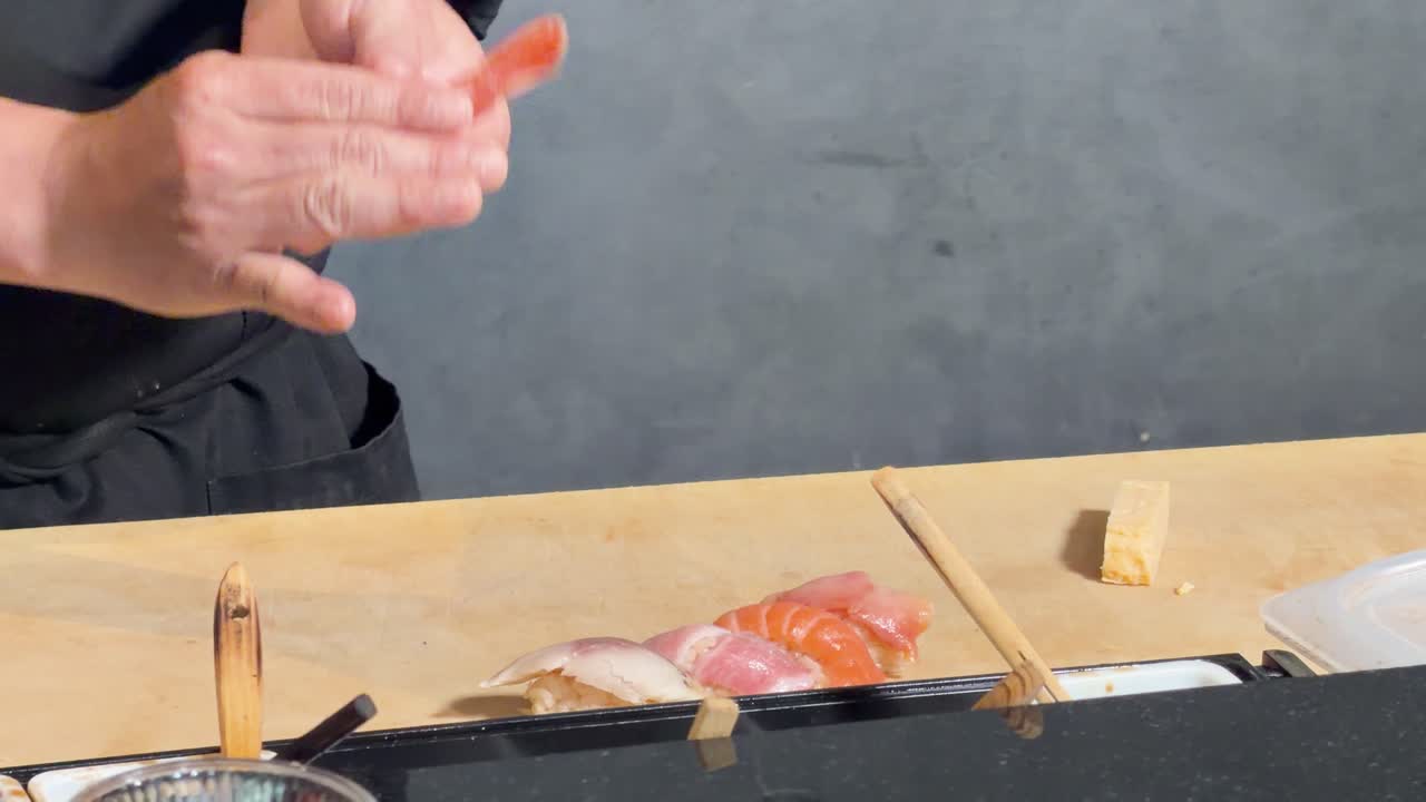 Detailní záběr profesionálního šéfkuchaře, který tvaruje krevety nigiri sushi na dřevěném pultu pod jemným osvětlením