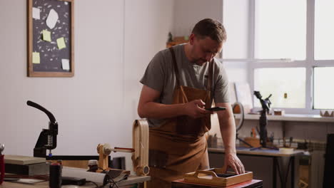 master takes picture of leather item with smartphone in shop