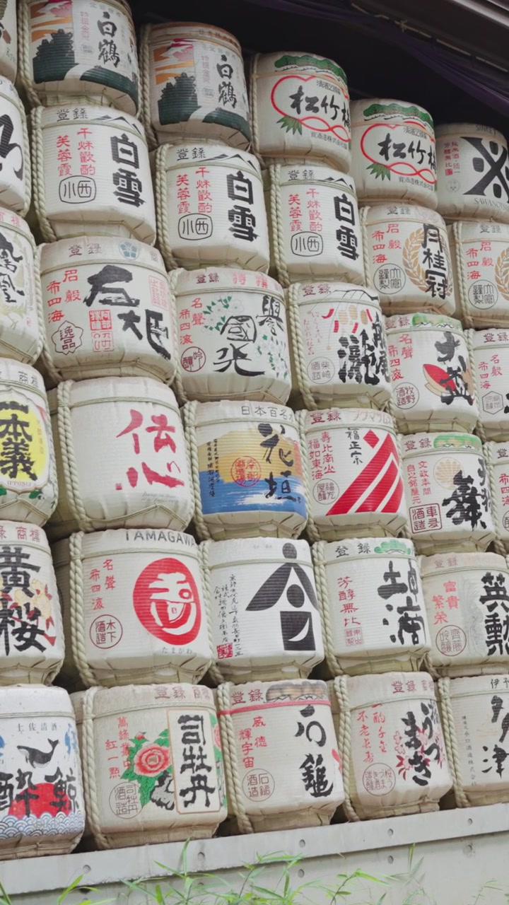 Vertical slow-motion video of the colorful and beautiful sake barrels at Meiji Jingu Shrine during the daytime in Yoyogi Park in Tokyo.