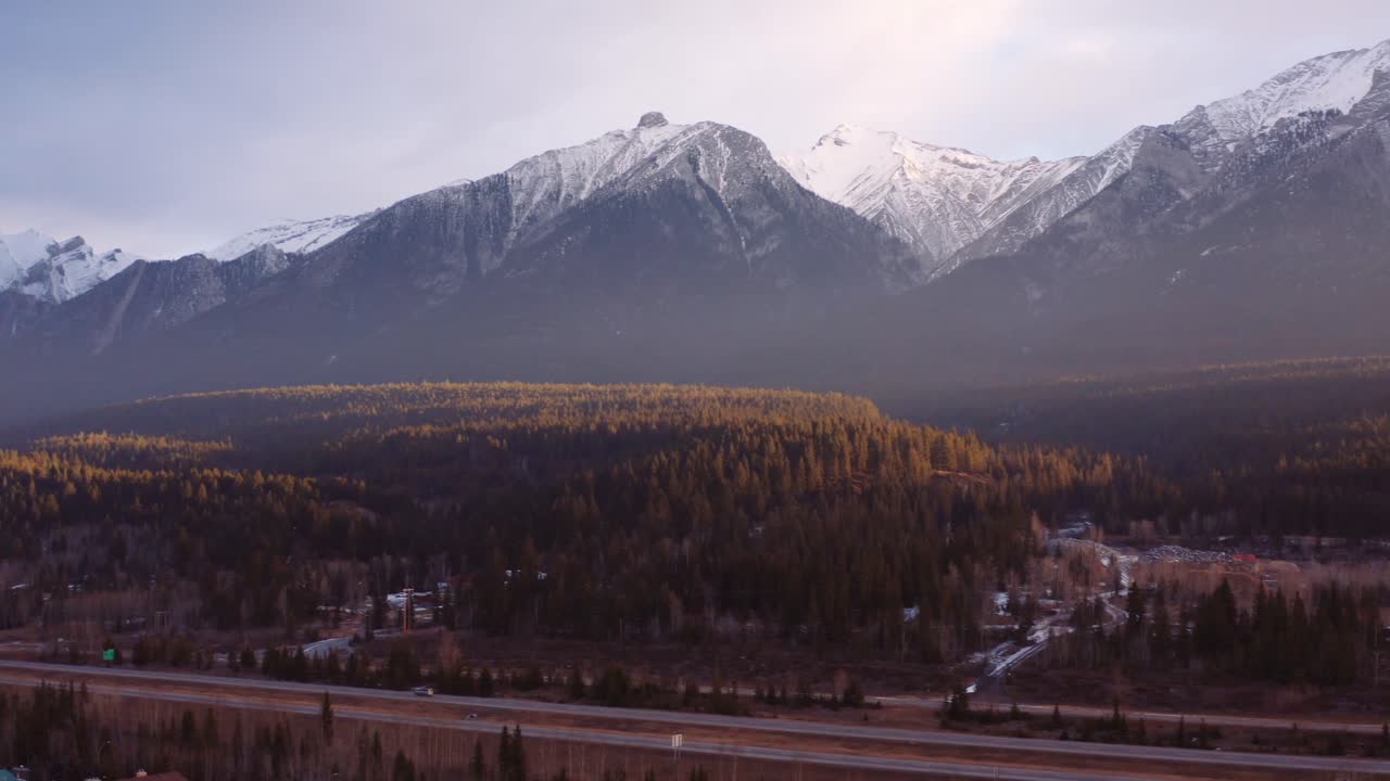 canmore alberta cordillera montañas rocosas canadienses fondo aéreo amanecer disparo de drones, grúa por carretera con autos conduciendo, gran complejo de condominios en primer plano