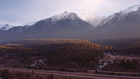 Canmore,-Alberta,-Cordillera-De-Las-Montañas-Rocosas-Canadienses,-Tiro-Aéreo-Del-Dron-Del-Amanecer,-Grúa-Por-La-Carretera-Con-Los-Coches-Que-Pasan,-Gran-Complejo-De-Condominios-En-Primer-Plano