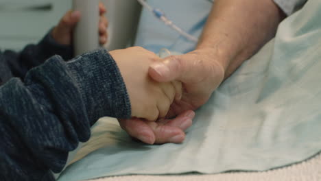 little boy holding grandmothers hand granny lying in hospital bed child showing affection at bedside for grandparent recovering from illness health care family support