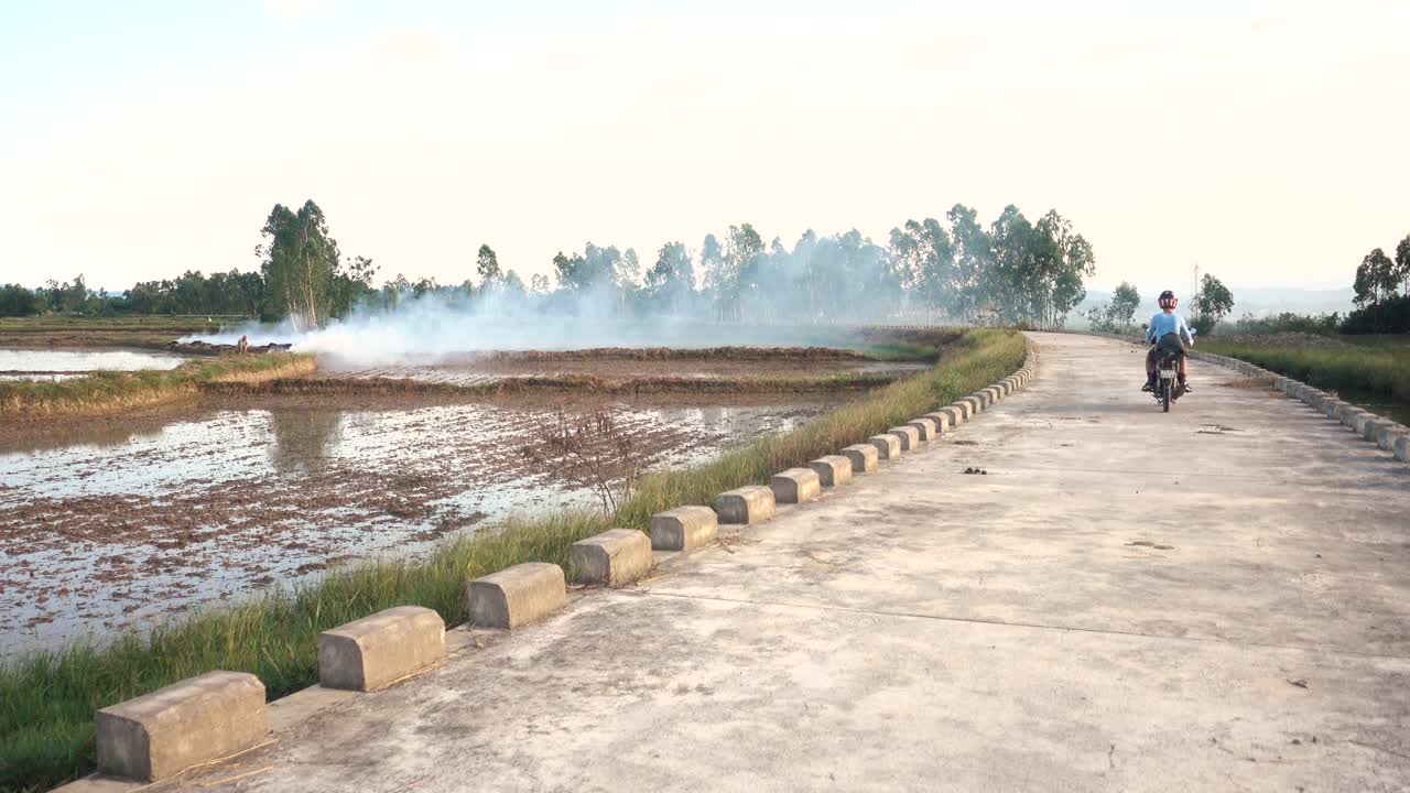 Person riding motorbike on rural road through rice paddies