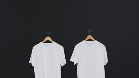 Video-Von-Zwei-Weißen-T-Shirts-Auf-Kleiderbügeln-Und-Kopierraum-Auf-Schwarzem-Hintergrund