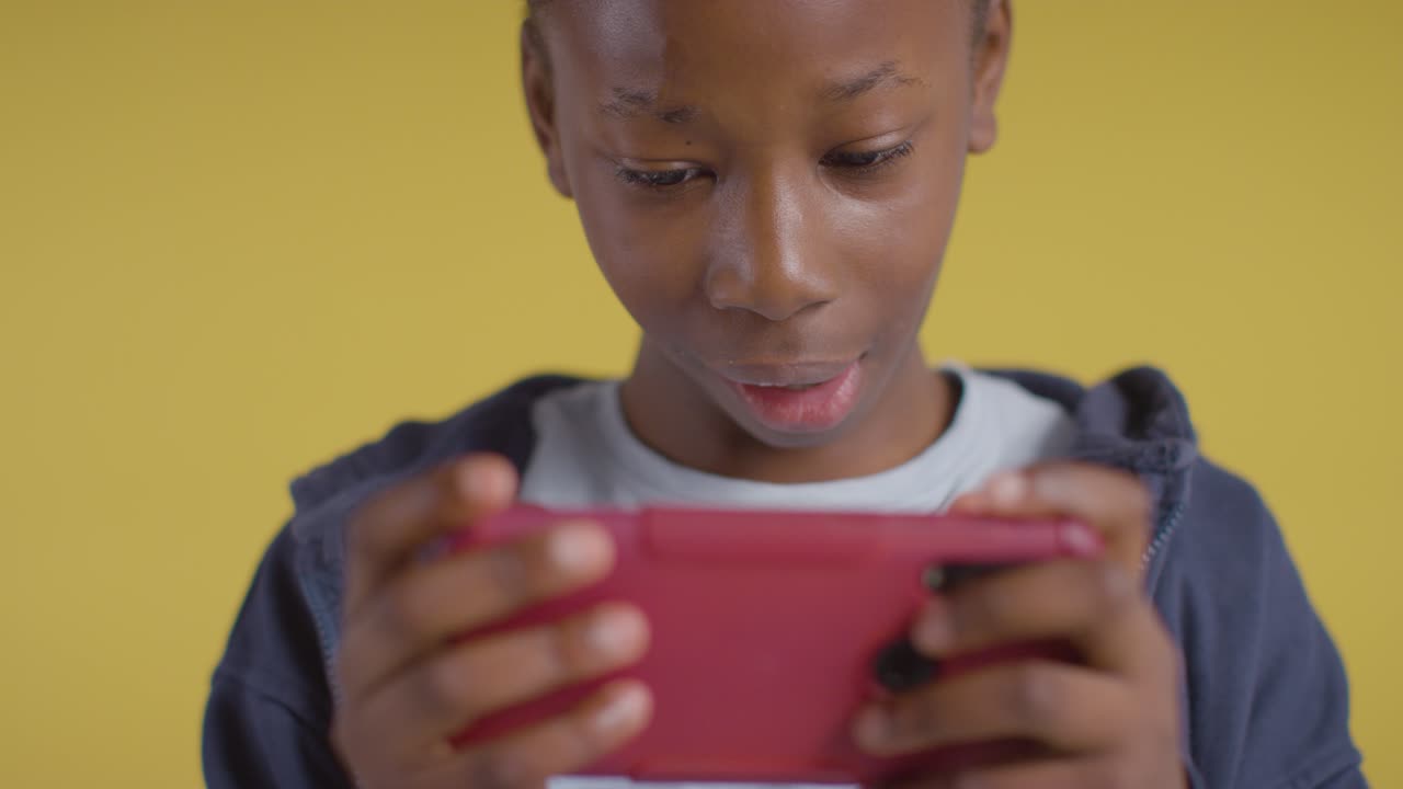Close Up Of Excited Boy On ASD Spectrum Gaming On Mobile Phone On Yellow Background 