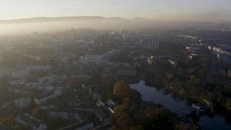 Drohnenaufnahme-Der-Stadtlandschaft-Von-Kassel-In-Schönem,-Weichem-Sonnenlicht-Und-Mit-Nebel-Bedeckt