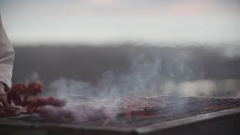 blurred close up of chef grilling meat skewer outdoors moroccan street food in front of beautiful ocean