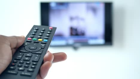 mano sosteniendo un control remoto de tv frente a una pantalla de tv