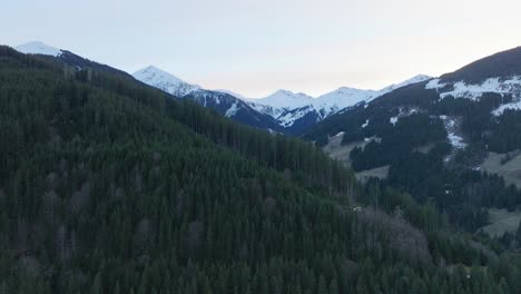 Kiefernwald-Bedeckt-Berge-Mit-Schneeflecken-In-Saalbach-Hinterglemm-In-Der-Abenddämmerung,-Luftaufnahme