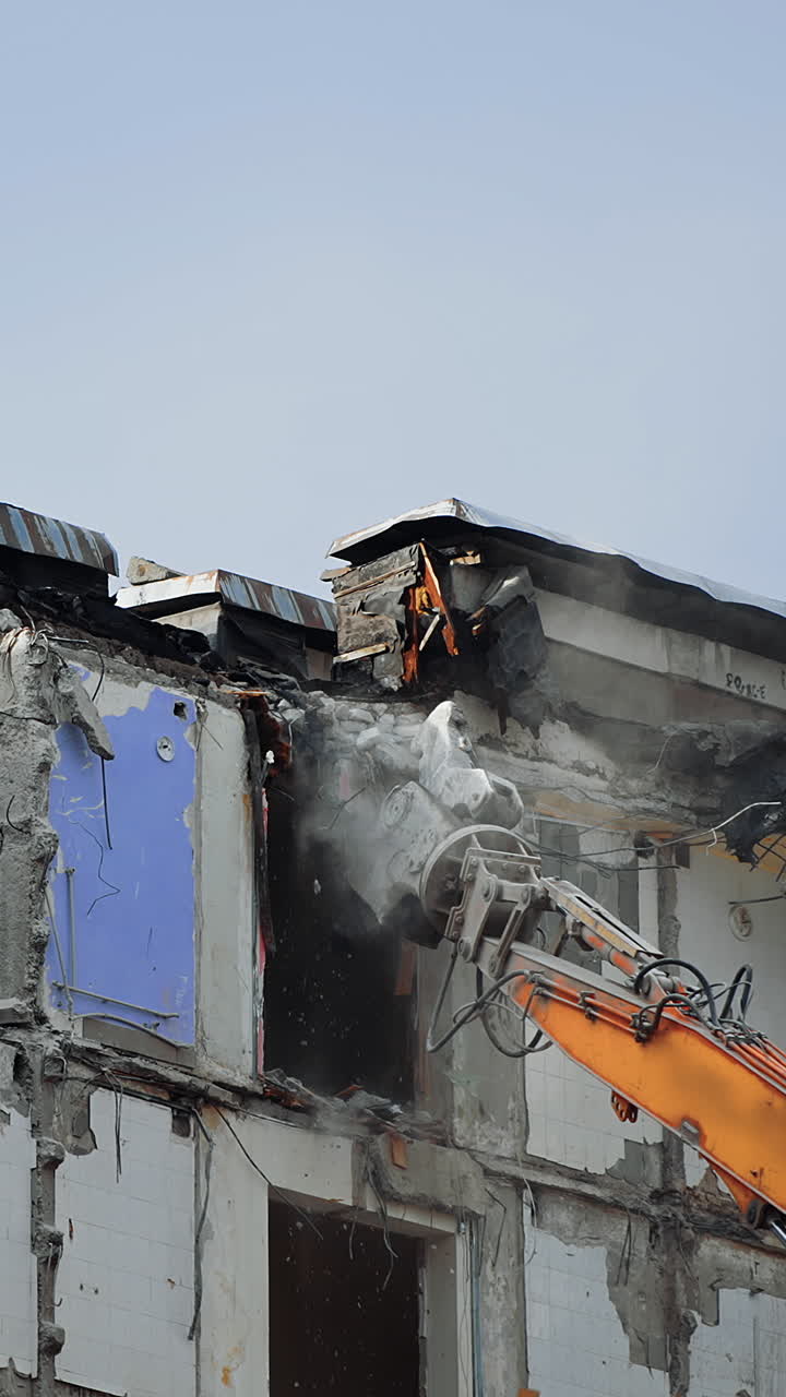 Destruction machine demolishes the ruined building. Pieces of concrete falling down from the roof of the destroyed house. Cleaning the site for the new construction. Vertical video