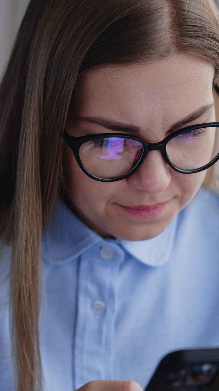 Concerned long-haired woman looking on the phone she's holding in both hands. Worried lady reading news on the smartphone. Vertical video