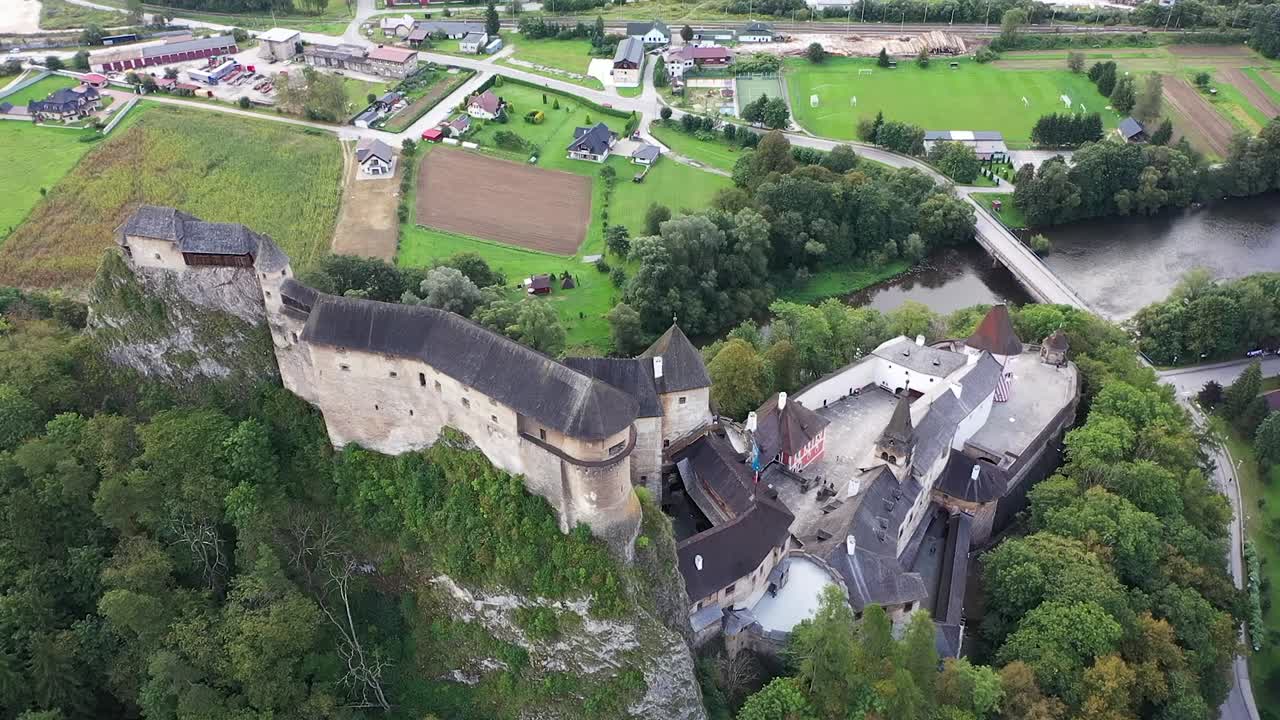 A drone descends beside Orava Castle, smoothly lifting the camera to reveal its soaring towers, stone walls, and the majestic Slovak landscape unfolding below