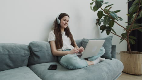 Cute-Young-Female-Makes-A-Video-Call-With-Her-Laptop-From-The-Sofa-At-Home