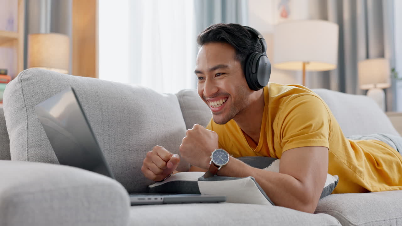 노트북, 헤드폰, 스포츠를 가진 소파에 앉아 있는 남자