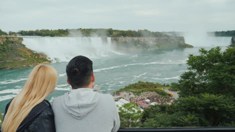 Vista-Desde-La-Parte-Posterior-De-Una-Joven-Pareja-Multiétnica-Mirando-Las-Famosas-Cataratas-Del-Niágara-En-Canadá