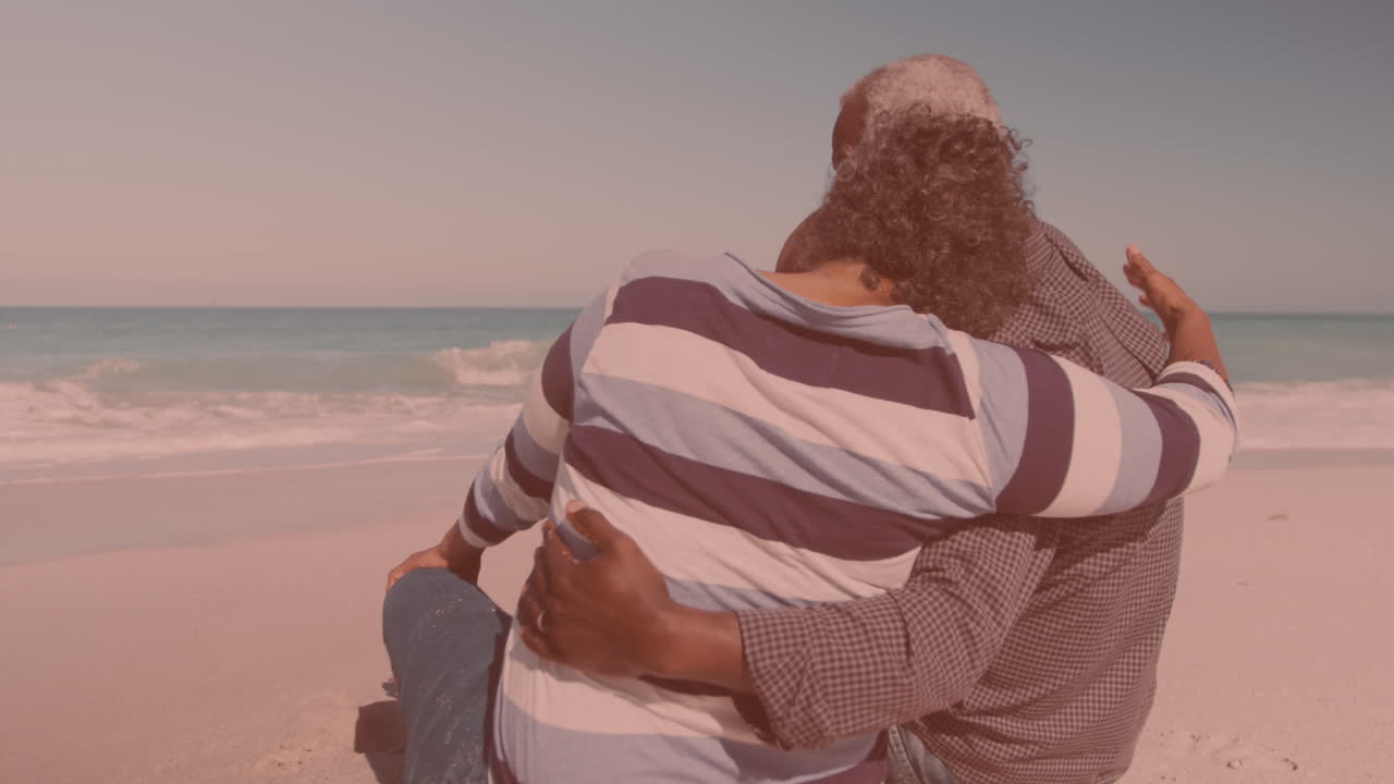 Rear view of african american couple hugging each other while sitting at the beach