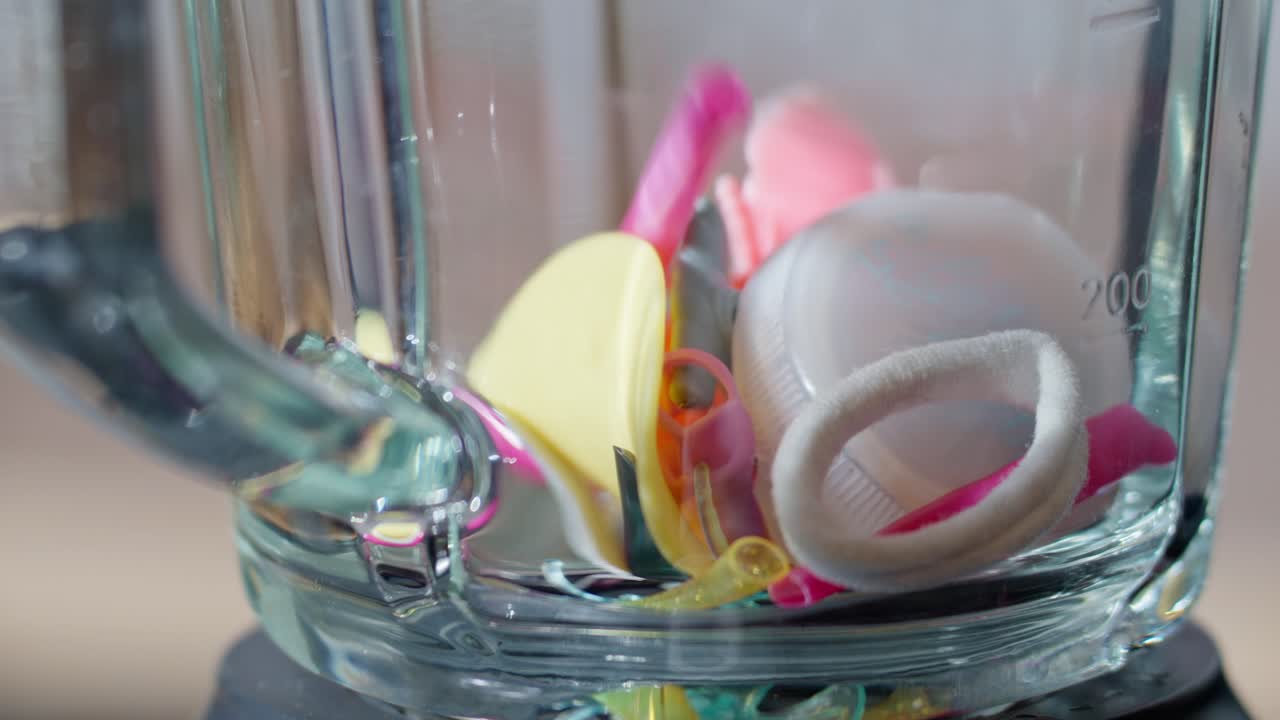 플라스틱 물건들이 빈 블렌더에 느리게 떨어지면서 과도한 사용과 미래의 폐기물을 강조합니다.