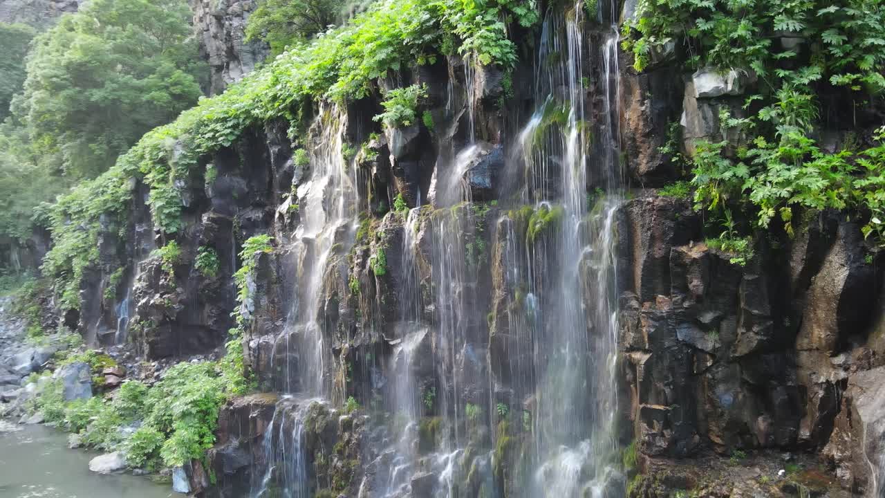 una impresionante cascada que cae en cascada por un acantilado rocoso, rodeada de una vibrante vegetación verde, creando una pintoresca y refrescante escena natural
