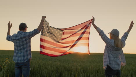 a happy couple raises up the us flag, standing against the backdrop of a wheat field at sunset.