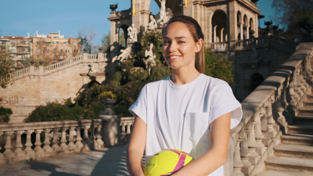 손에 공을 들고 도시 공원에서 행복하게 카메라를 바라보는 스포츠 여성.