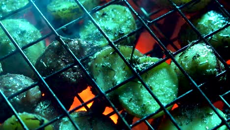 primer plano de patatas nuevas con hierbas en una cesta de alambre en una parrilla caliente con brasas rojas brillando debajo