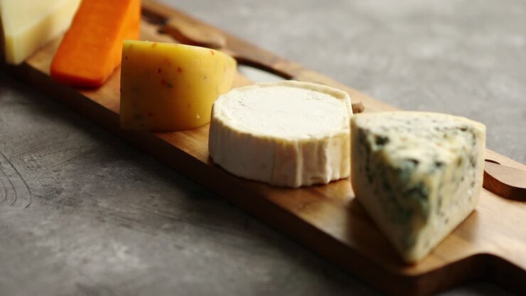 Assortment of various kinds of cheeses served on wooden board with fork and knives