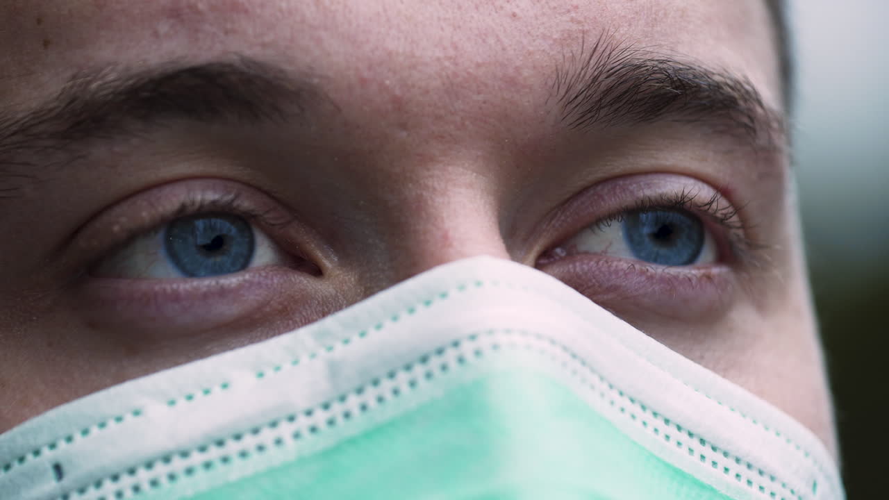 un giovane con occhi azzurri luminosi, che indossa una semplice maschera protettiva verde covid-19 che guarda in lontananza con speranza e aspettative, primo piano statico 4k shot