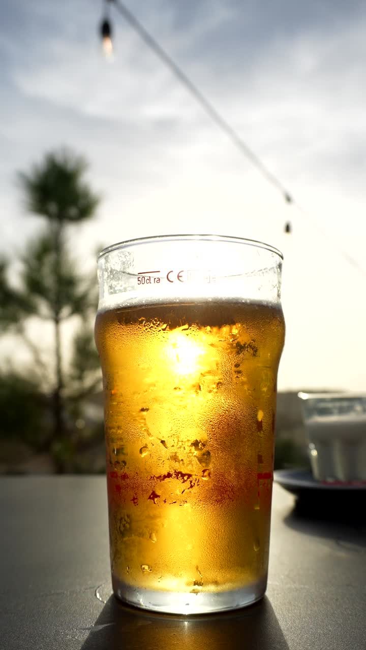 Mano che afferra un bicchiere di birra freddo al tramonto