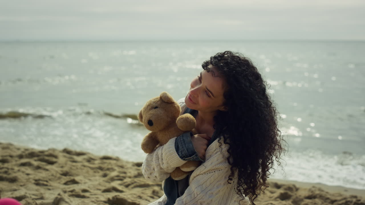 Donna latina posa sulla spiaggia del mare. Splendida signora modella tenendo un orsetto di peluche all'aperto.