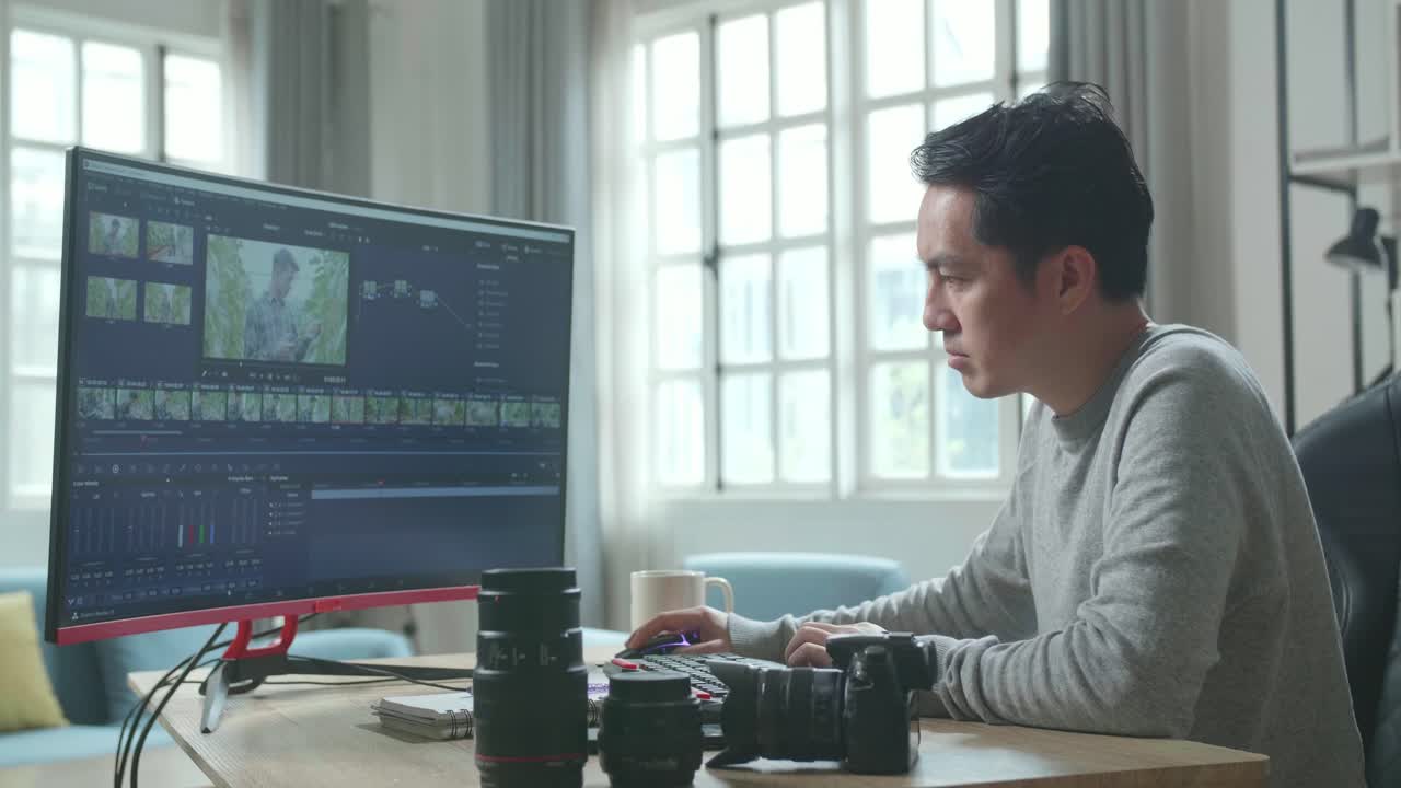Asian Video Editor Or Colorist Man In Long Sleeved T-Shirt Using Desktop Computer For Editing Video While Working At Home.