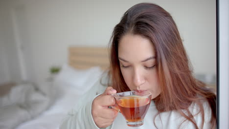 thoughtful plus size biracial woman having tea in bedroom, looking up, copy space, slow motion