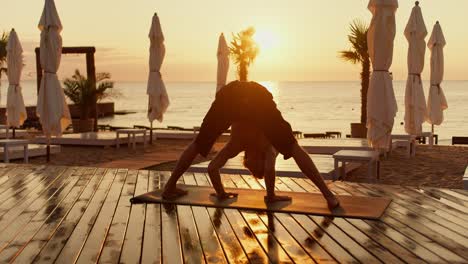 the guy gets on his head in a special yoga exercise on the beach in the morning. yoga classes at dawn healthy lifestyle