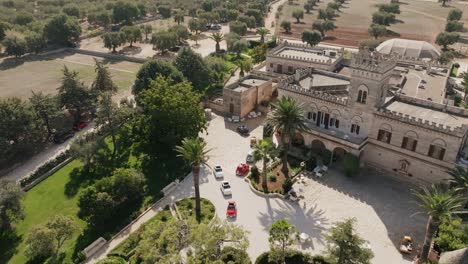 aerial footage rotating around the front parking lot of a masseria in southern italy with a lot of small colorful cars parked there