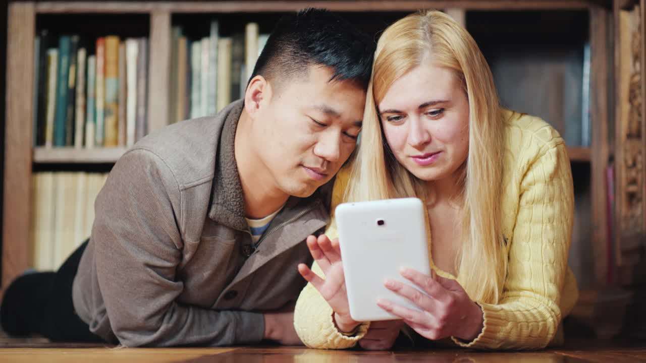 一对带着狗的年轻夫妇用平板电脑躺在地板上