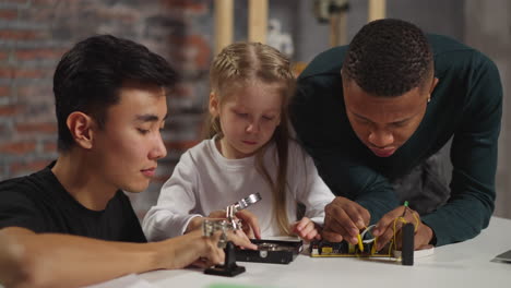 Little girl looks at fixed device with engineer and teacher