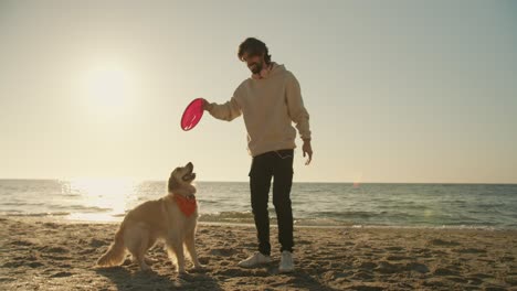 El-Tipo-Juega-Con-Un-Juguete-Rojo-Con-Su-Perro-De-Color-Claro-En-Una-Playa-Soleada-Por-La-Mañana