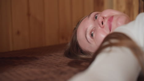 close up of girl lying on bed, hand extended feeling soft texture of material, thoughtfully gazing upwards, serene and reflective moment in cozy indoor environment with warm wood backdrop