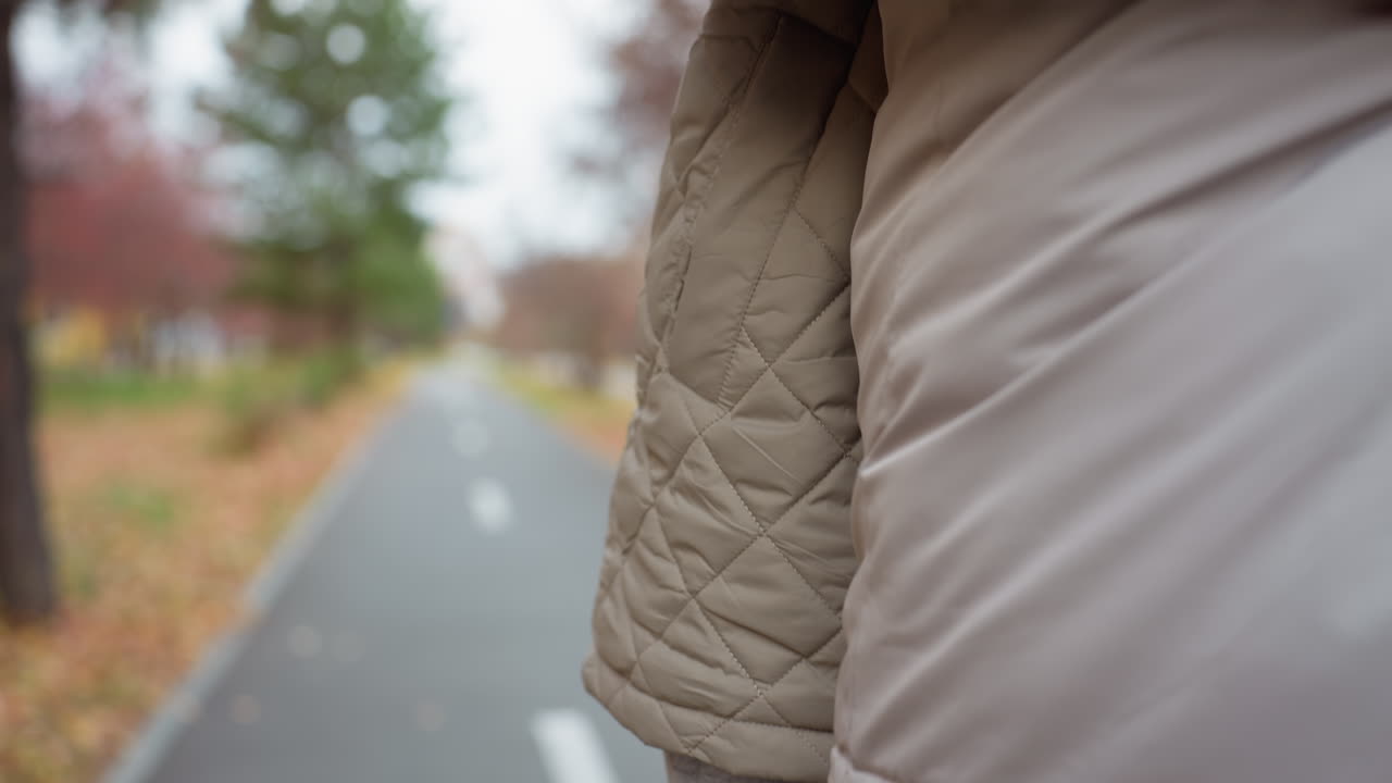 Close up rear view of woman with vibrant purple nails walking to meet her fiance as they prepare to hug warmly on autumn path dressed in same outfit with foliage scattered along calm park trail