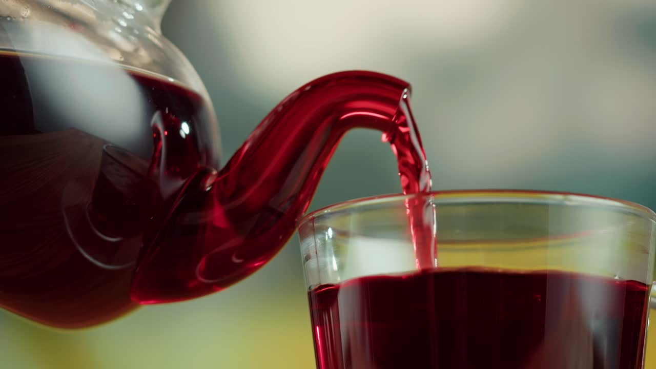 Pouring Red Tea from a Glass Teapot into a Cup