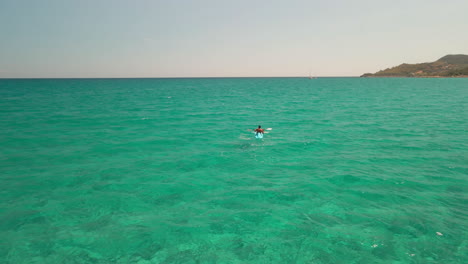 Rückansicht-Des-Mannes-Auf-Dem-Kajak,-Der-Allein-Im-Klaren-Blauen-Meer-Unter-Der-Augustsonne-In-Sardinien,-Italien-Segelt---Drohnenaufnahme-Aus-Der-Luft