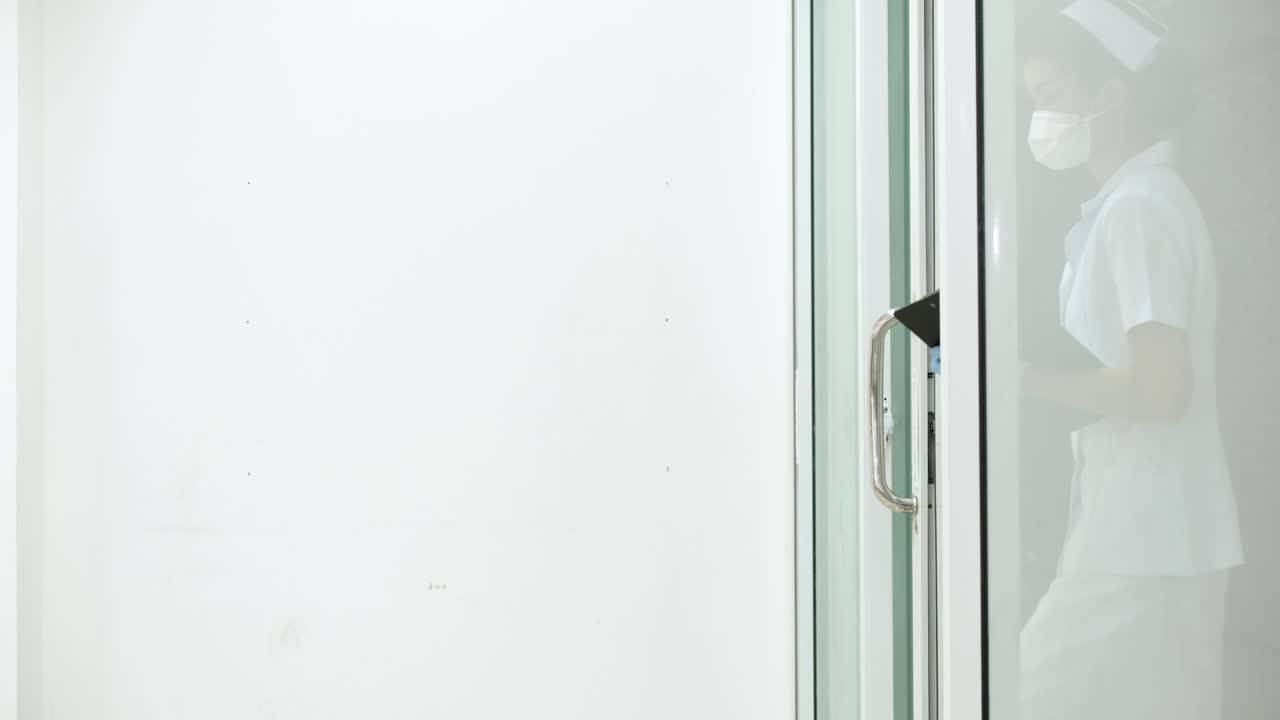 매력적인 아시아 간호사가 병원에서 문을 열고 환자를 돕기 위해 대기실로 걸어갑니다.