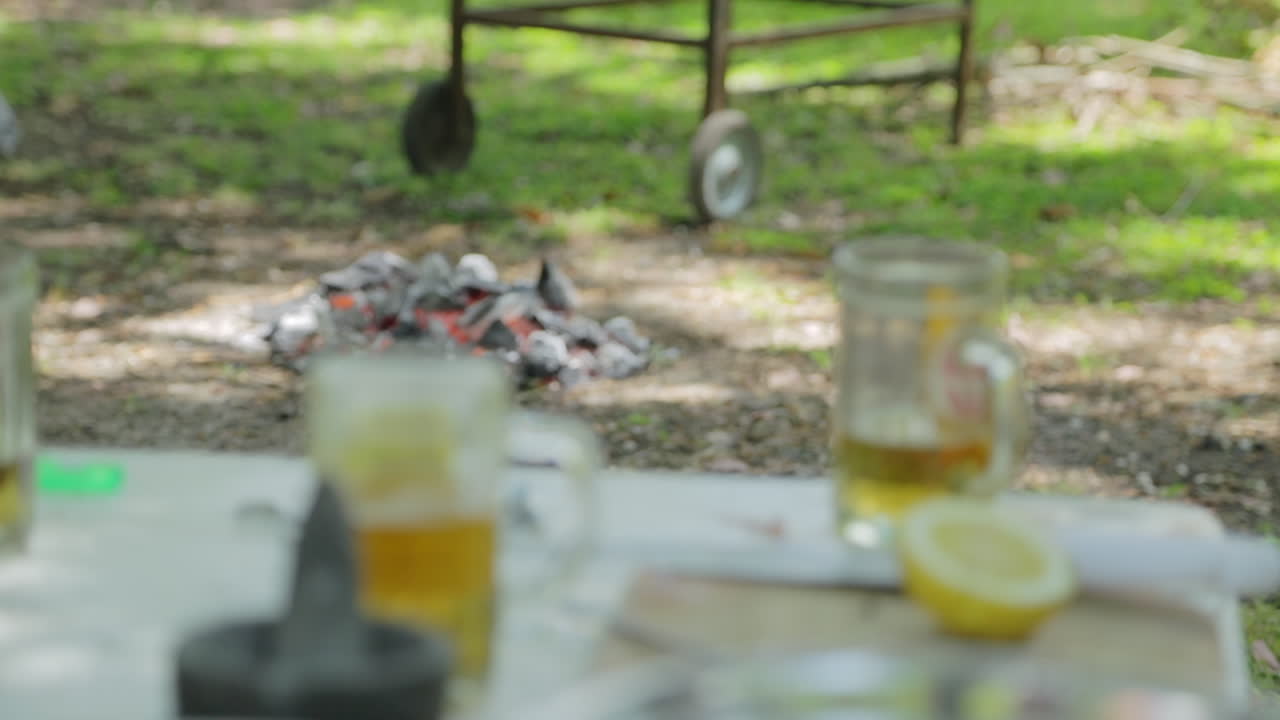 cerca de las cervezas y la preparación de alimentos en la mesa de picnic con barbacoa y fuego en el fondo