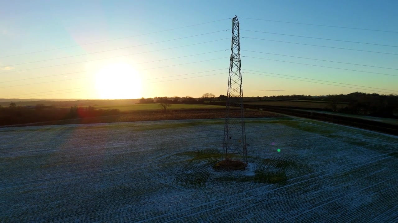 Aerial view of high-voltage pylons in frost covered snow fields at sunset, UK.