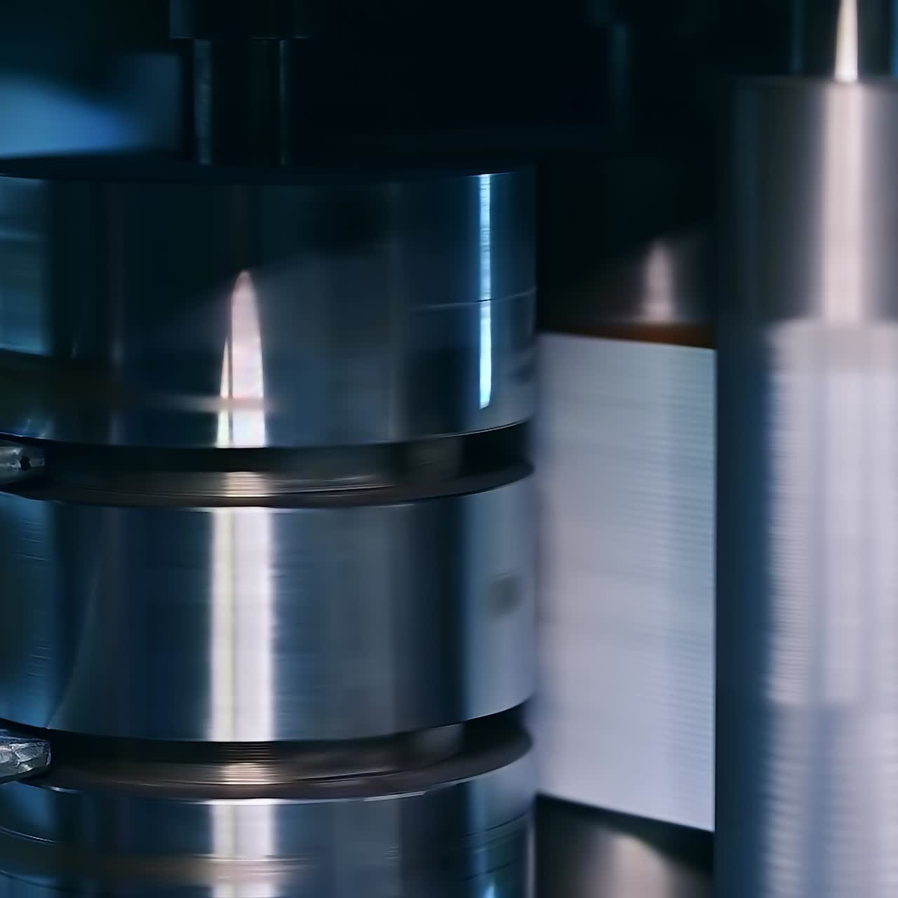 Shining metal vertical shaft spinning fast and moving a roll of fiber for future diapers. At the factory producing nappies