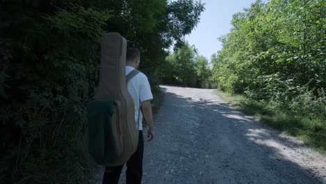 young man walking with guitar on street near forest