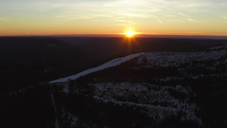 Toma-Panorámica-Aérea-Sobre-Una-Pista-De-Esquí-Al-Amanecer-En-La-Cima-De-Una-Montaña-Nevada-Del-Bosque-Negro-Con-Tiempo-Despejado