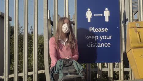 woman wearing mask looking in bag near to social distancing sign wide shot