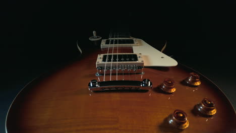 Slow-tracking-up-the-body-of-a-Gibson-Les-Paul-electric-guitar,-covering-the-volume-and-tone-controls,-bridge,-guard,-pickups-and-strings