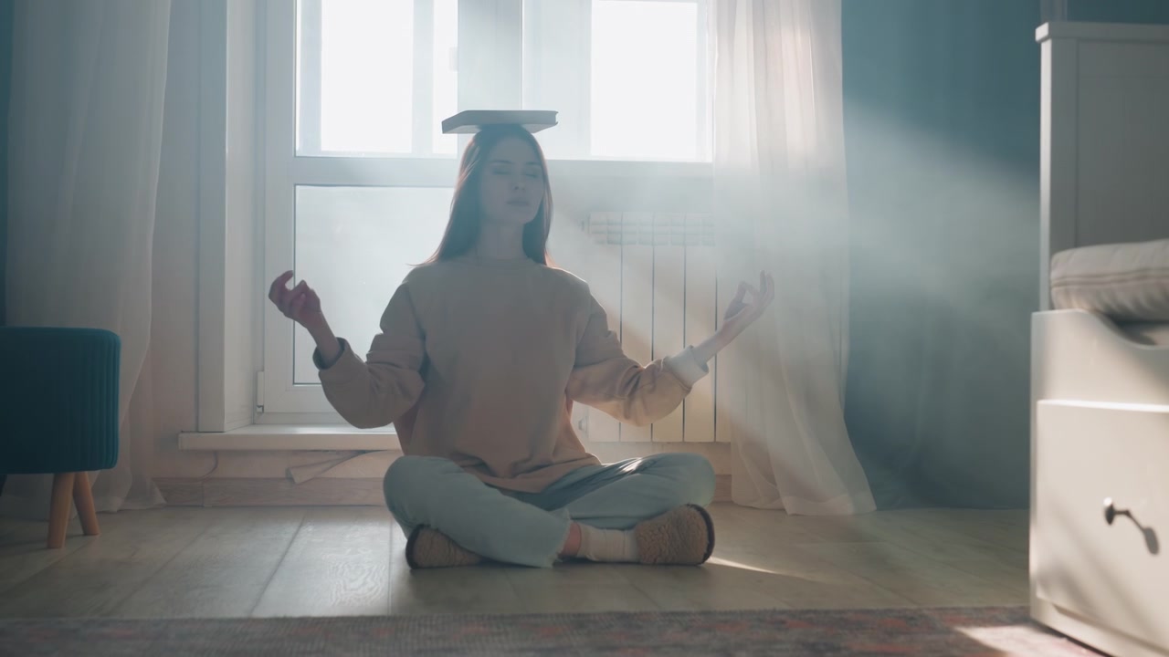 Jovem mulher equilibrando um livro na cabeça, no chão ensolarado do quarto, tutora particular praticando postura e respiração com um sorriso calmo, cortinas e tapete macios, suéter aconchegante, sentada de pernas cruzadas, raios suaves.