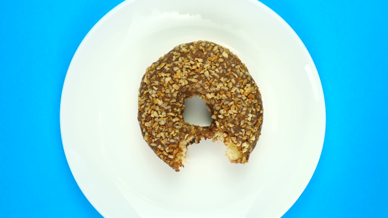 dulce rosquilla mordida gira en un plato. aislado en azul, vista de arriba